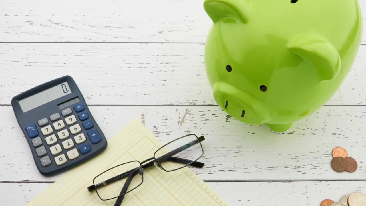 Calculator, glasses, coins and a green piggy bank on a desk
