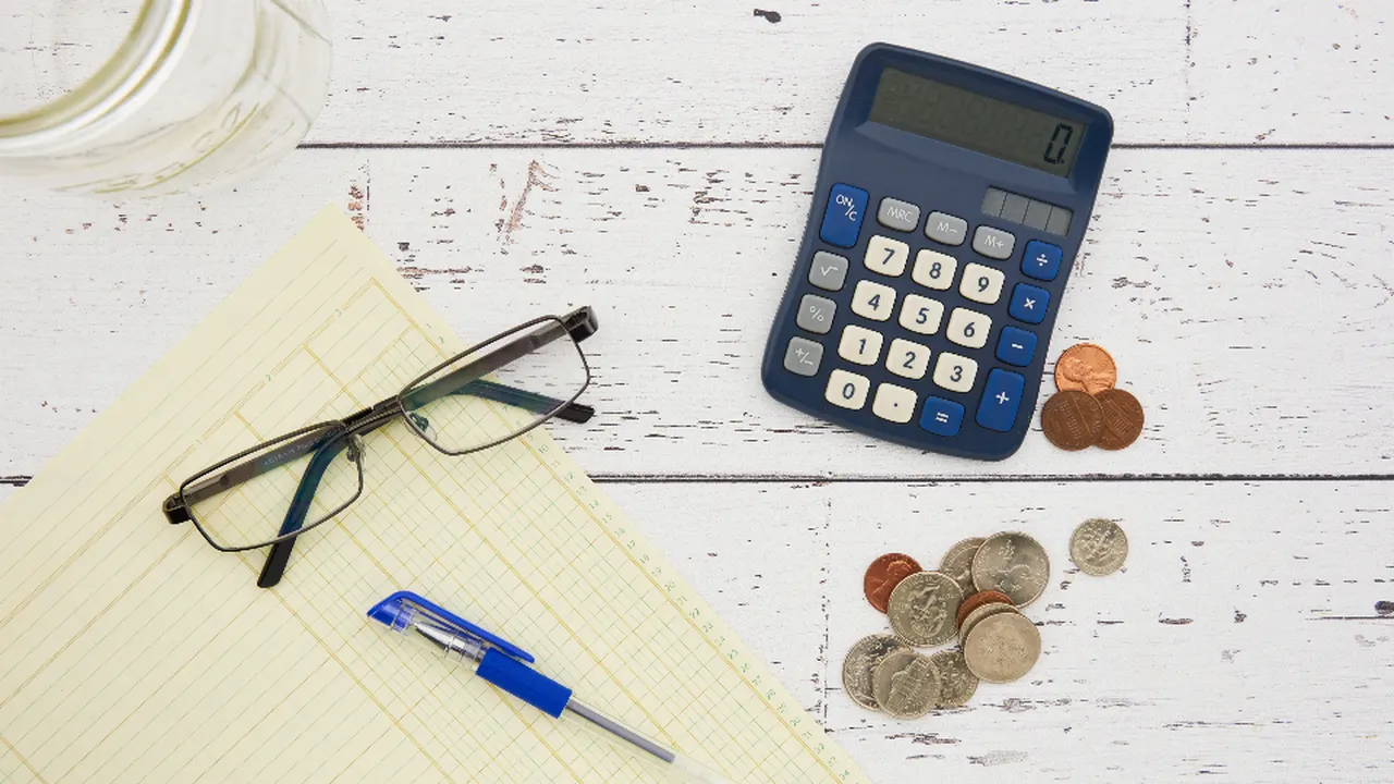 Calculator, coins, glasses and a pen on a white desk