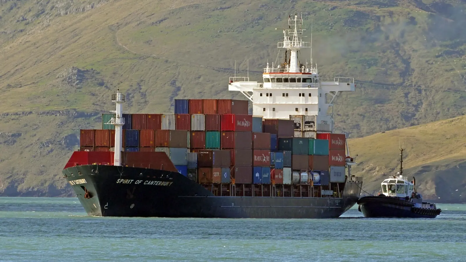 Loaded container ship sailing with a tugboat alongside