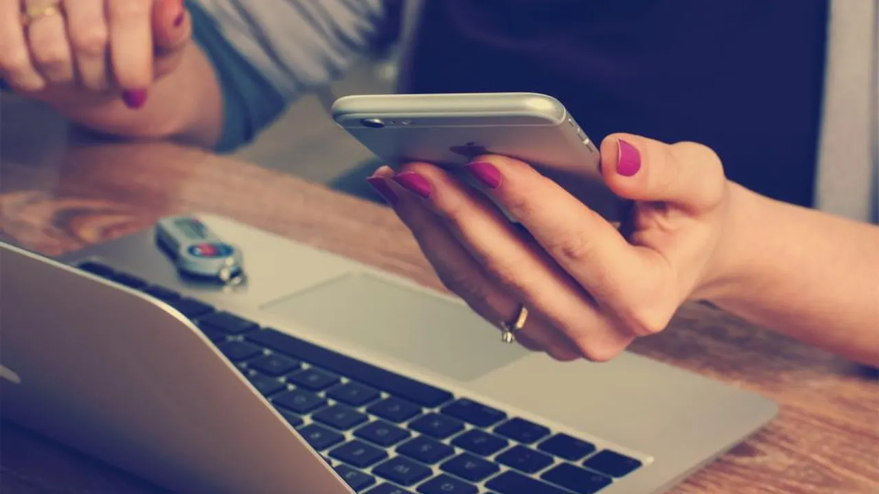 Person using a phone next to a laptop